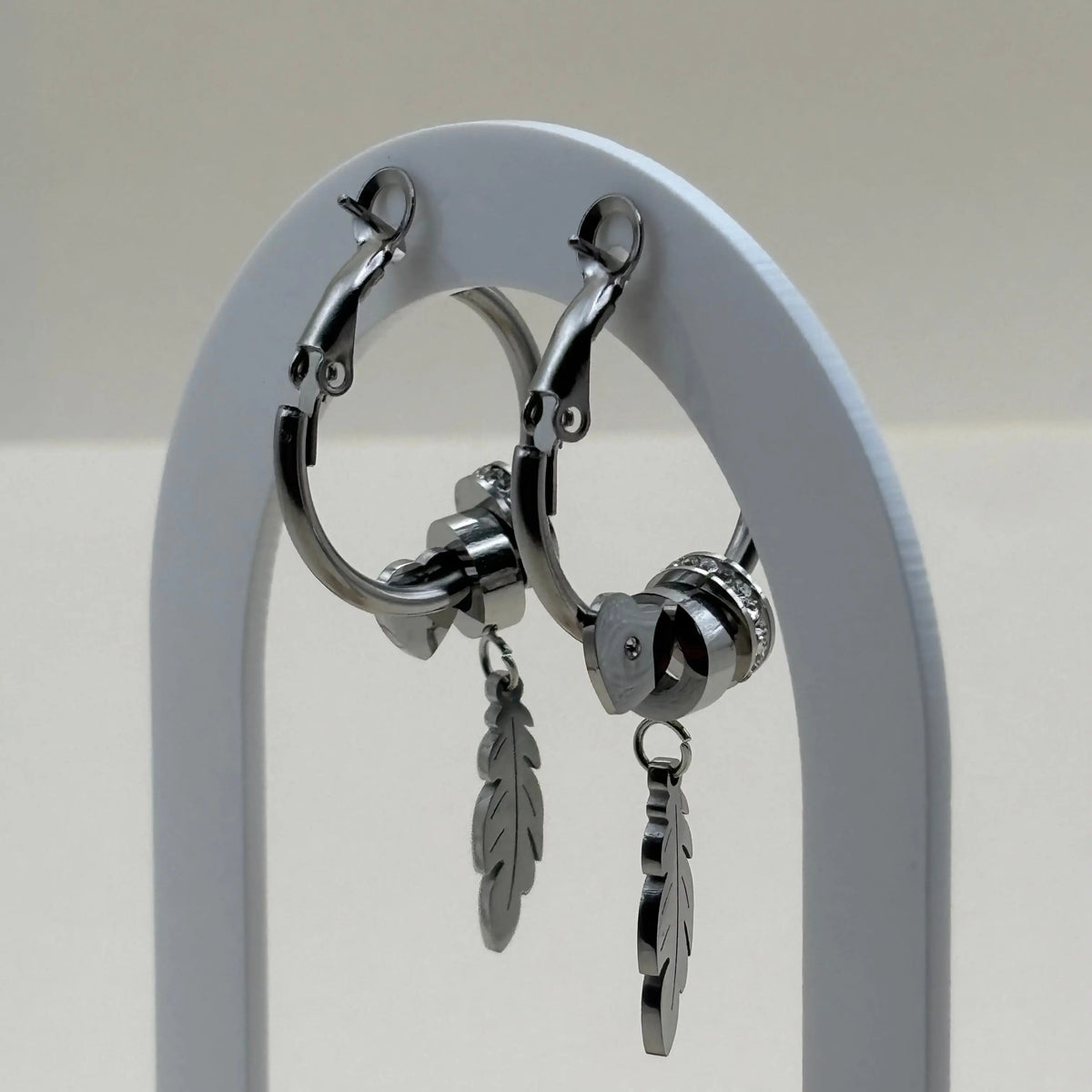 Une paire de boucles d'oreilles créoles argentées avec motif plume et strass argent en acier inoxydable 