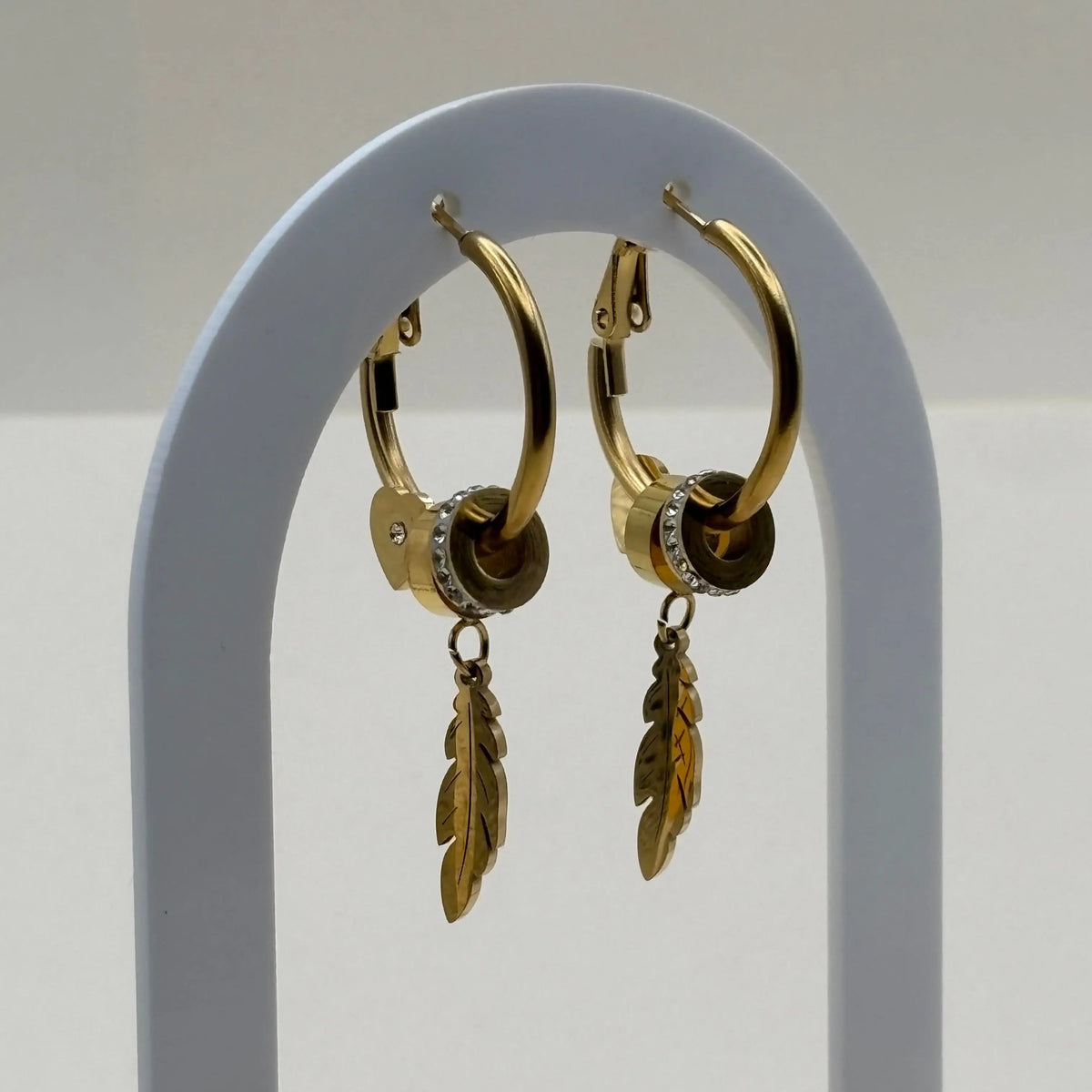 Des boucles d'oreilles créoles dorées avec motif plume et strass argent en acier inoxydable 