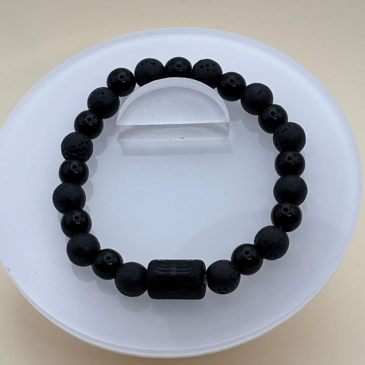 Bracelet formé de perles entièrement noires alternant textures mates et lisses avec un cylindre noir gravé en partie centrale