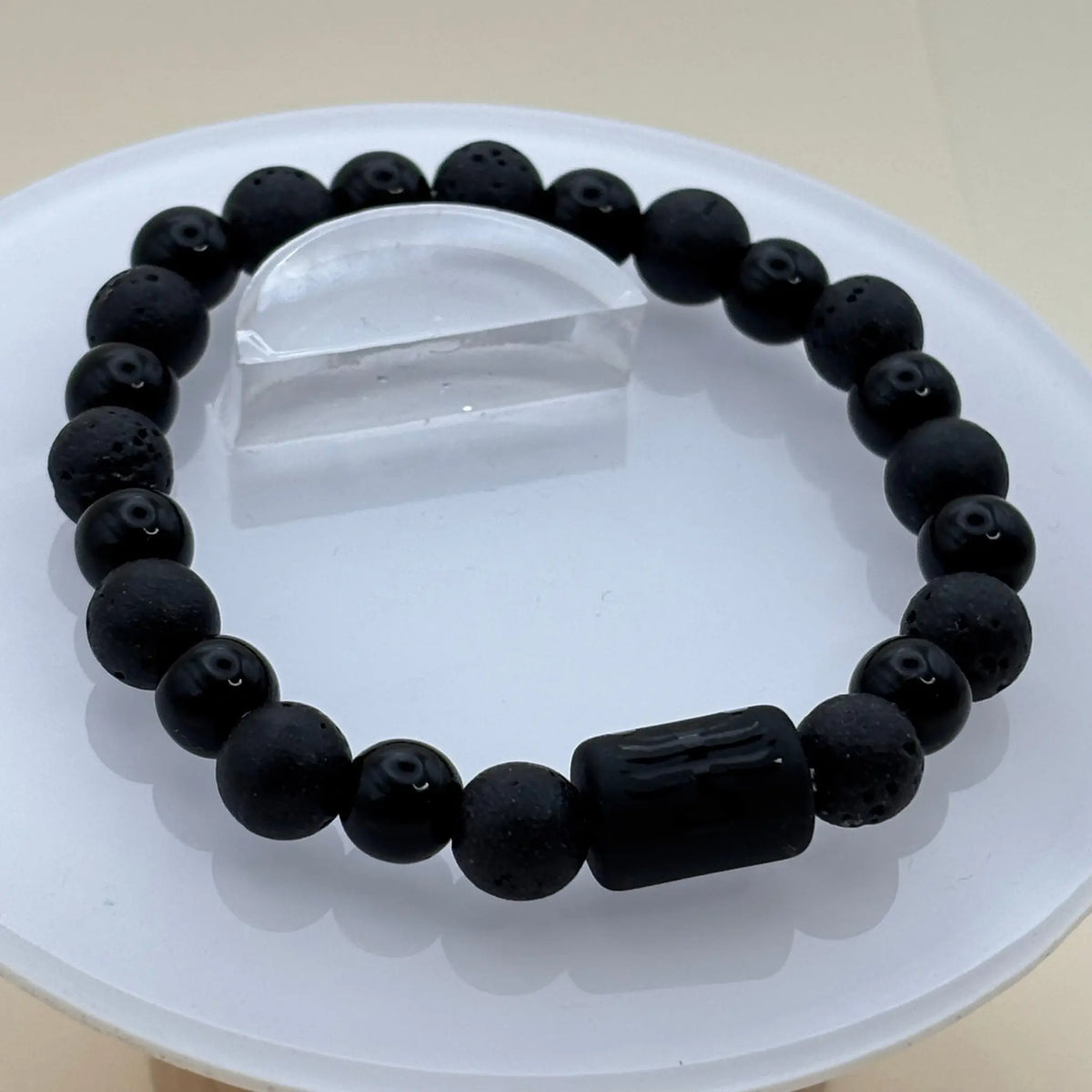 Bracelet en perles noires mates et brillantes disposant d’un cylindre noir gravé au centre