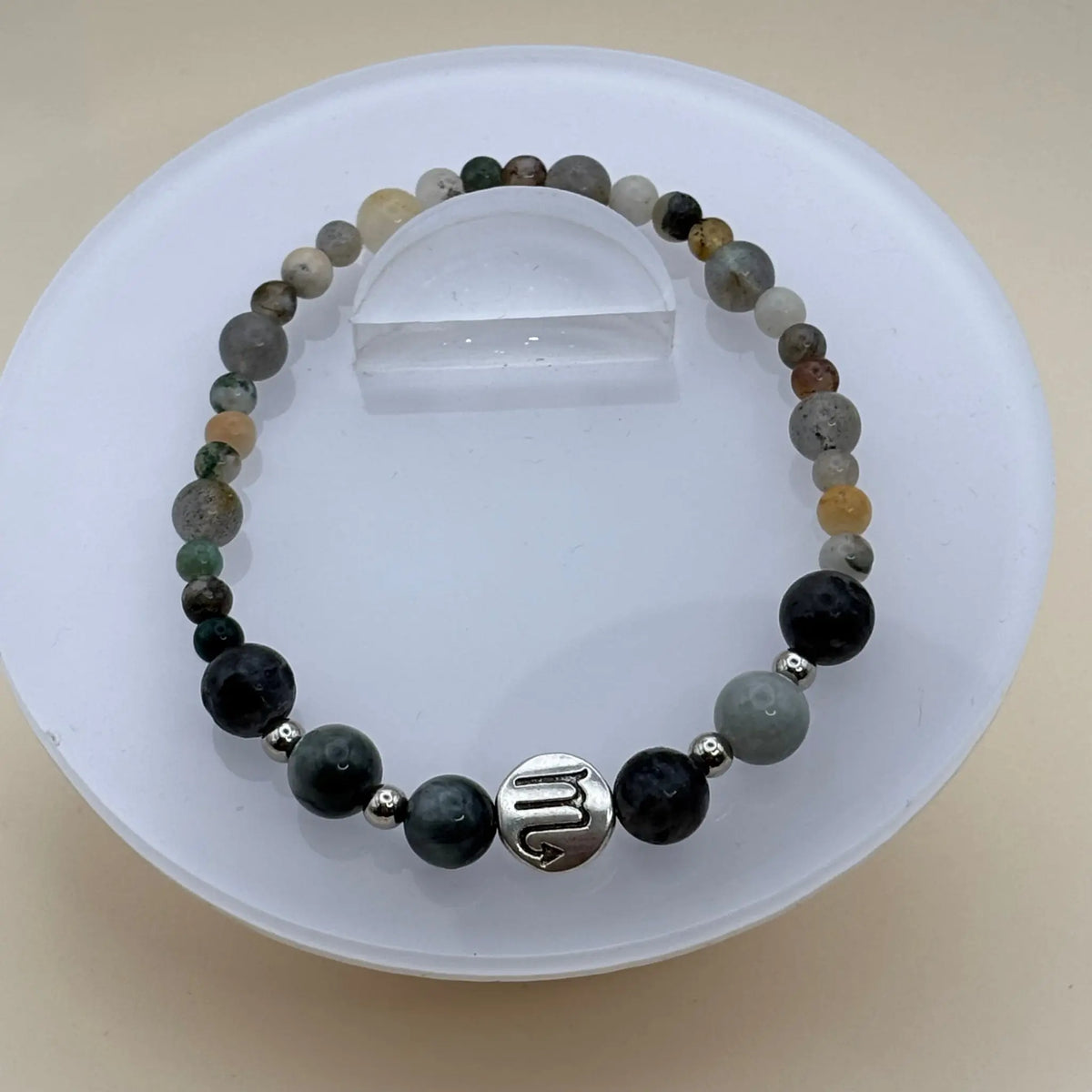 Bracelet aux perles multicolores dans des tons verts, gris et beige avec un médaillon argenté gravé au centre