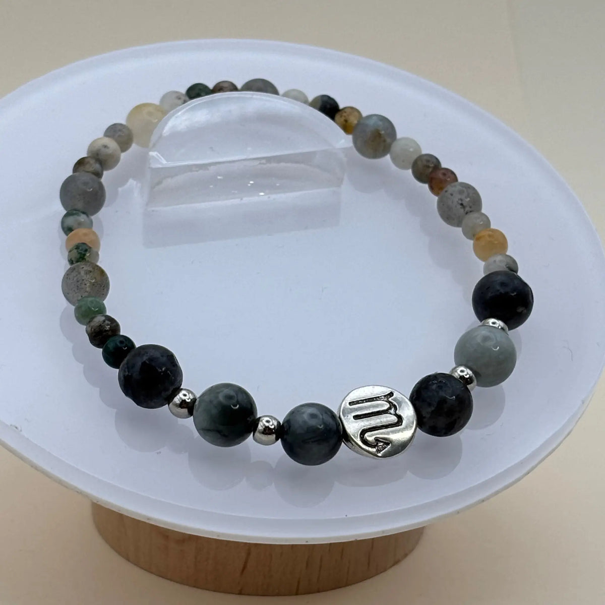 Bracelet aux perles variées gris, vert et beige décoré d’un médaillon argenté gravé positionné à l’avant