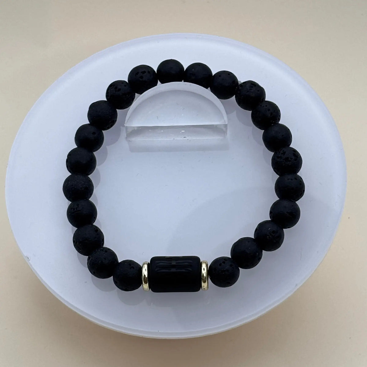 Bracelet aux perles noires mates et lisses accompagné d’un cylindre noir gravé entre deux anneaux dorés