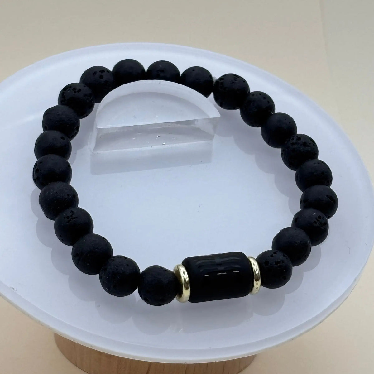 Bracelet de perles noires texturées rehaussé de deux anneaux dorés entourant un cylindre noir gravé