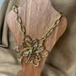 Vue de près d'un collier doré avec chaine grands maillons et pendentif en forme de fleur en acier inoxydable vendu sur le site internet prêtes à briller