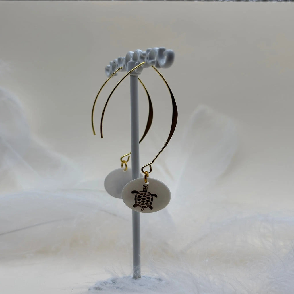 Une paire de boucles d'oreilles pendentif avec une pastille nacrée et dessin d'une tortue