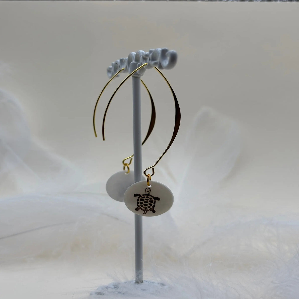 Une paire de boucles d'oreilles pendentif avec une pastille nacrée et dessin d'une tortue