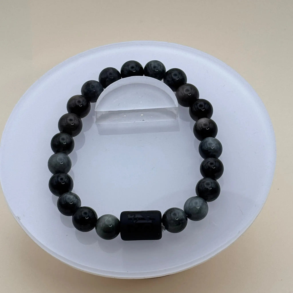 Bracelet formé de perles noires et grises foncées avec un cylindre noir gravé comme élément central