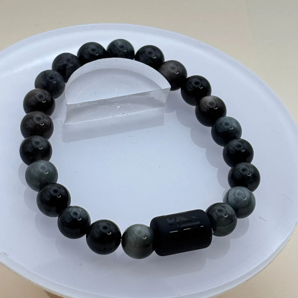 Bracelet composé de perles grises et noires avec un cylindre noir gravé situé au centre