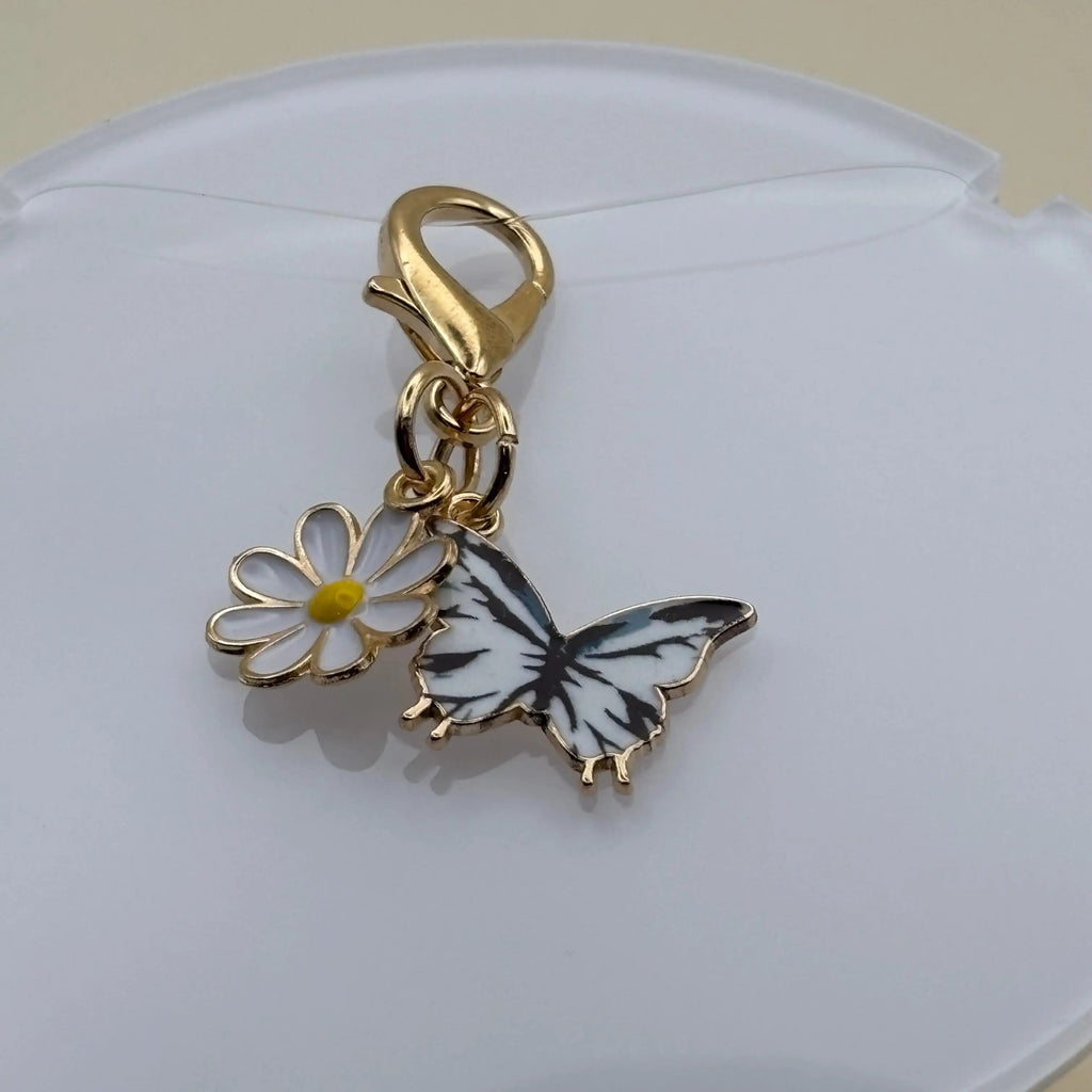 Bijou en acier à accrocher représentant un papillon blanc posé sur une marguerite, évoquant la légèreté, la nature et l’élégance florale.