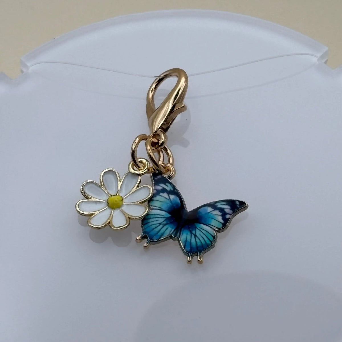 Bijou en acier à accrocher représentant un papillon bleu posé sur une marguerite, évoquant la légèreté, la nature et l’élégance florale.