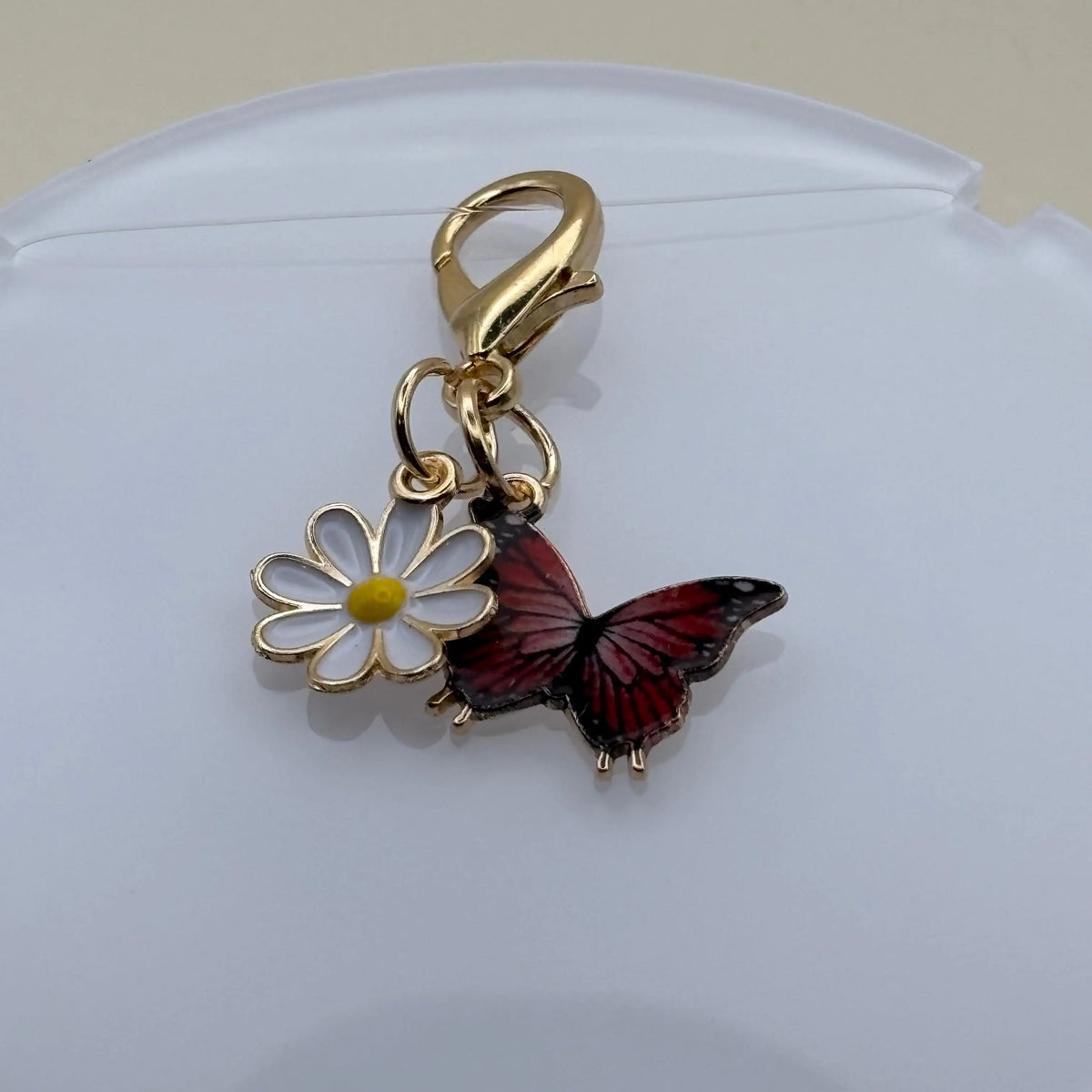 Bijou en acier à accrocher représentant un papillon noir posé sur une marguerite, évoquant la légèreté, la nature et l’élégance florale.