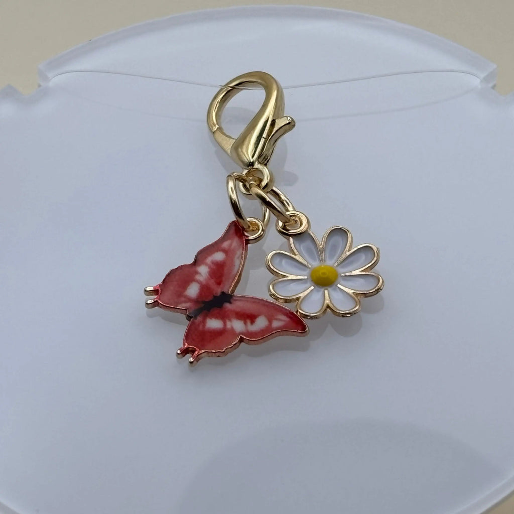 Bijou en acier à accrocher représentant un papillon rouge posé sur une marguerite, évoquant la légèreté, la nature et l’élégance florale.