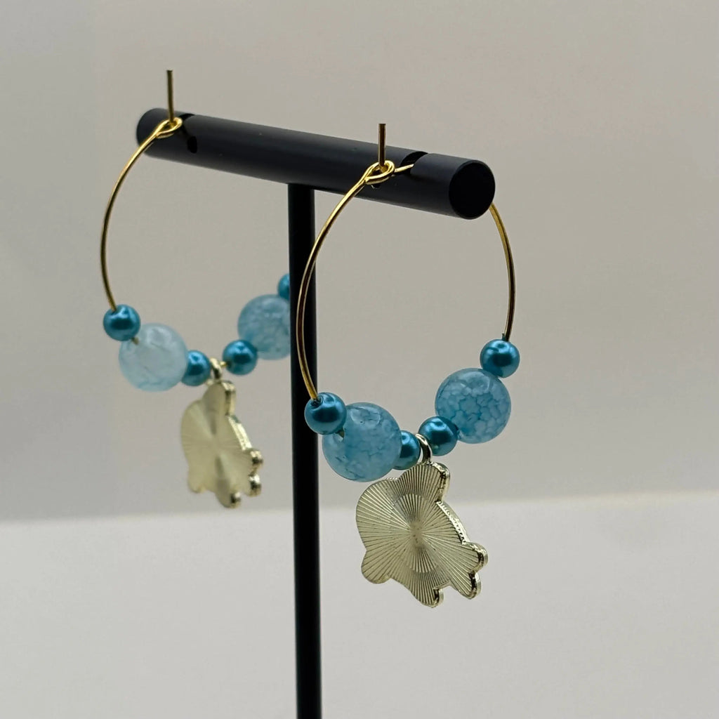 Une paire de boucles d'oreilles créoles dorées avec perles bleues clair et breloque baleine bleu et blanche 