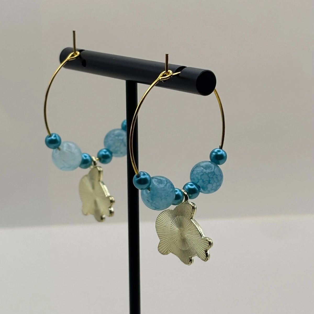 Une paire de boucles d'oreilles créoles dorées avec perles bleues clair et breloque baleine bleu et blanche 