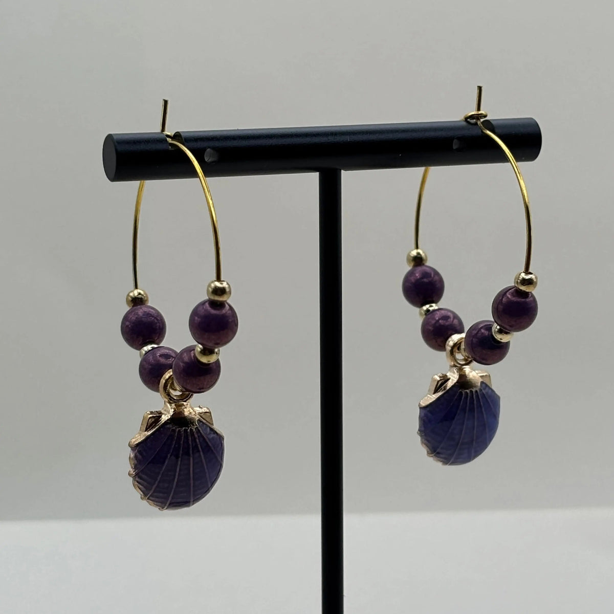 Des boucles d'oreilles créoles dorées avec perles violettes et breloque en forme de coquillage