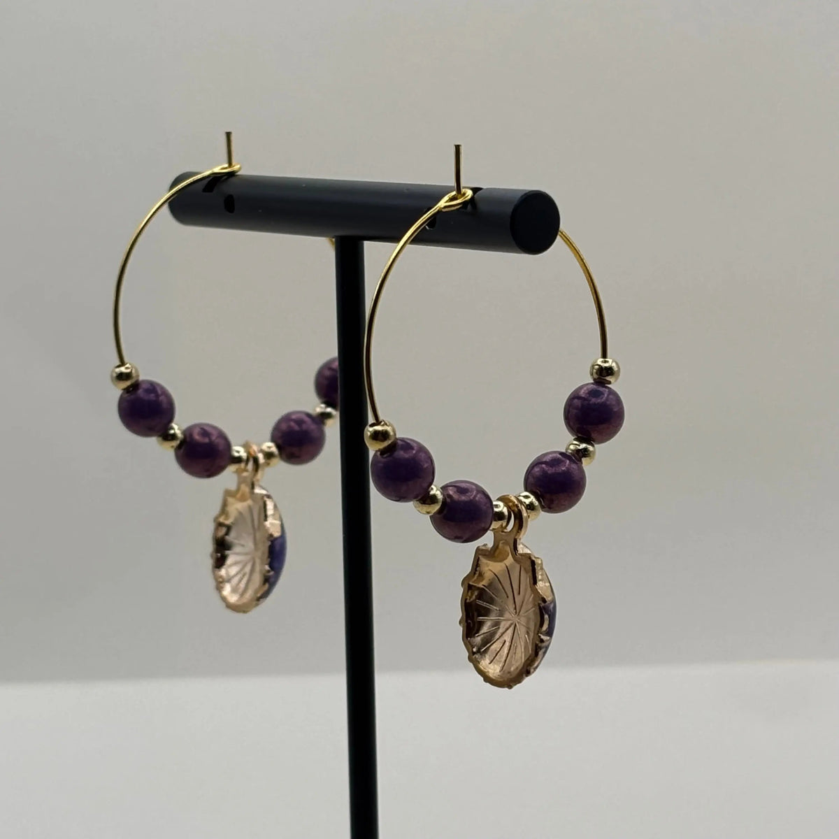 Une paire de boucles d'oreilles créoles dorées avec perles violettes et breloque en forme de coquillage