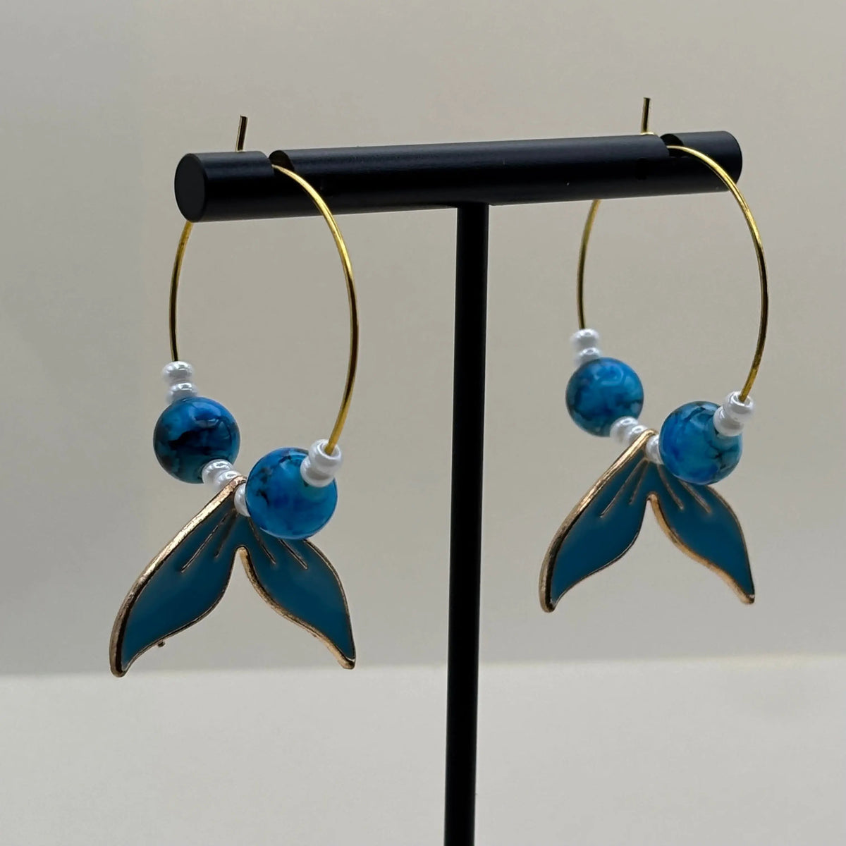 Des boucles d'oreilles créoles dorées avec perles bleues et breloque queue de baleine bleue
