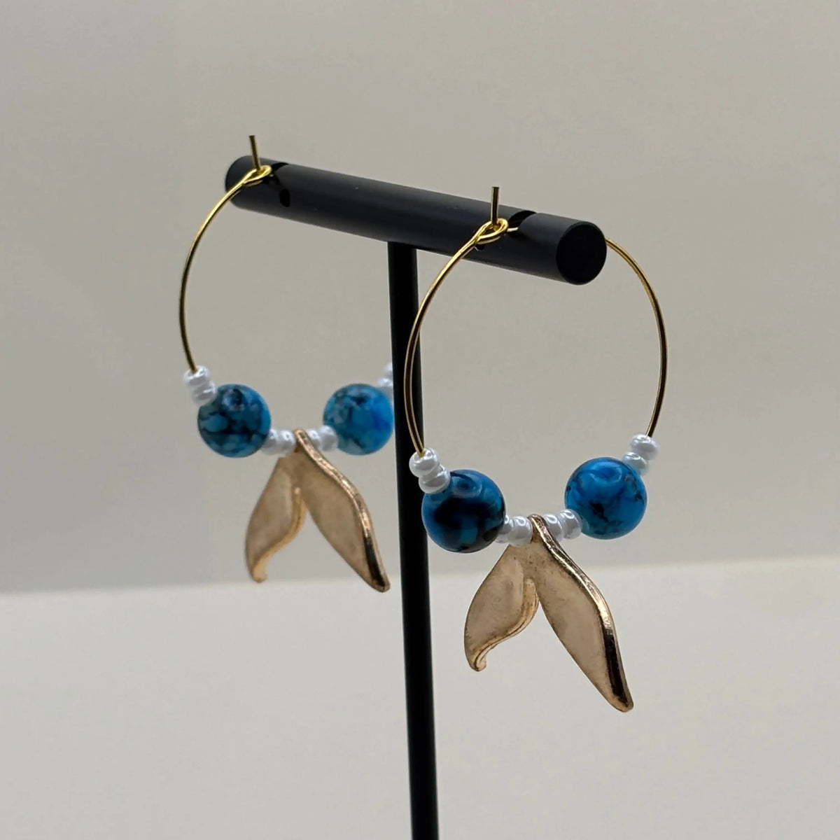 Une paire de boucles d'oreilles créoles dorées avec perles bleues et breloque queue de baleine bleue