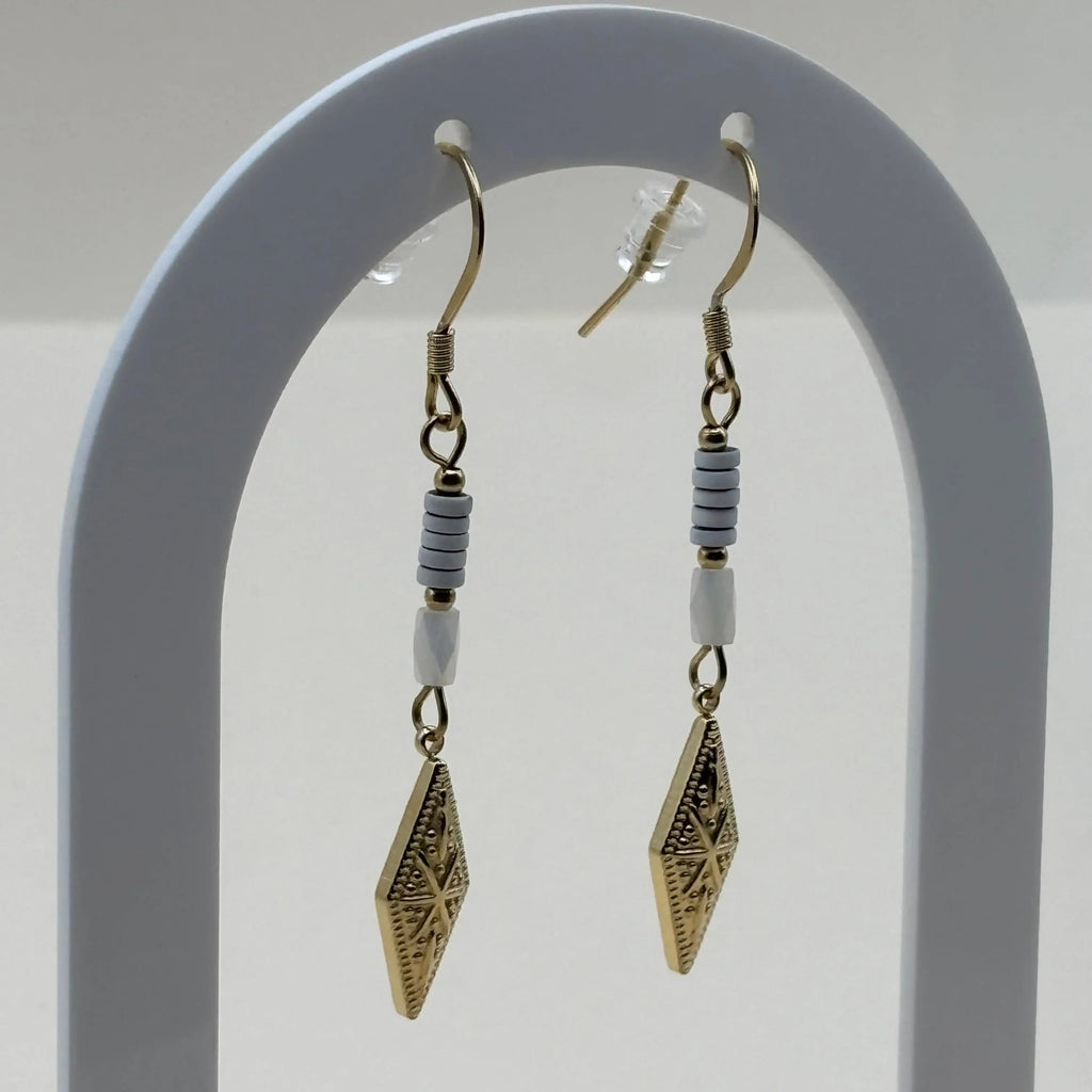 Des boucles d'oreilles pendentif dorées avec perles plates blanches et breloque dorée rose des vents