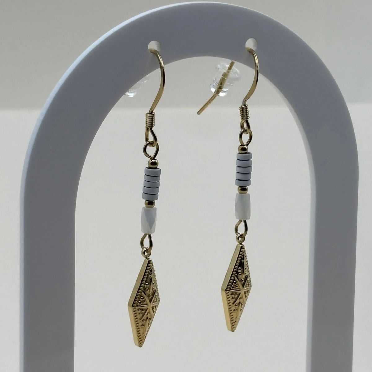 Des boucles d'oreilles pendentif dorées avec perles plates blanches et breloque dorée rose des vents