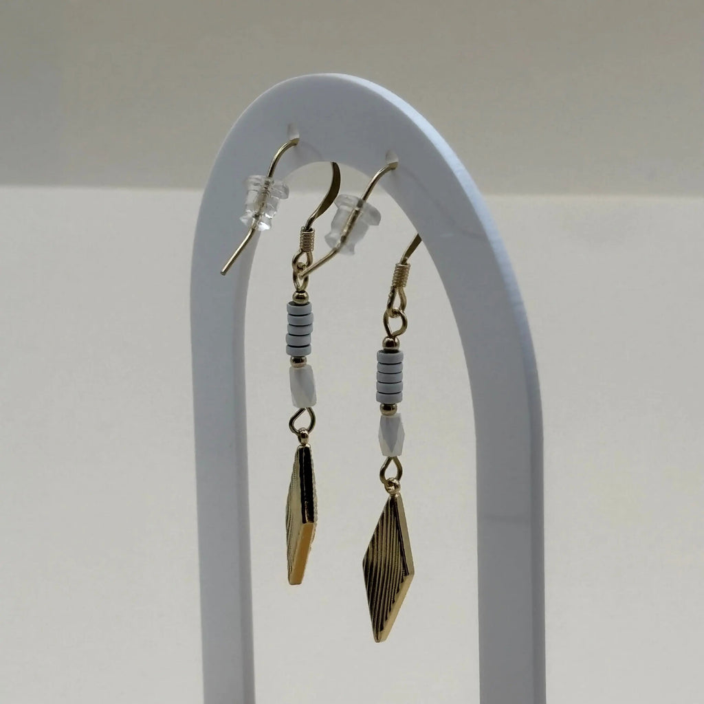 Une paire de boucles d'oreilles pendentif dorées avec perles plates blanches et breloque dorée rose des vents