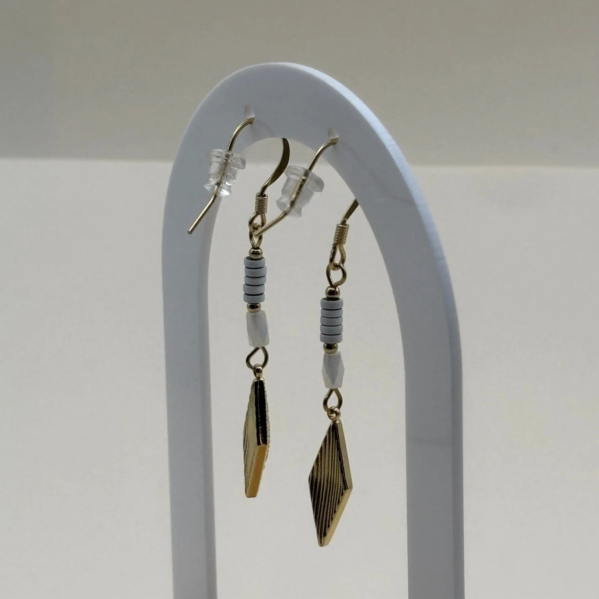 Une paire de boucles d'oreilles pendentif dorées avec perles plates blanches et breloque dorée rose des vents