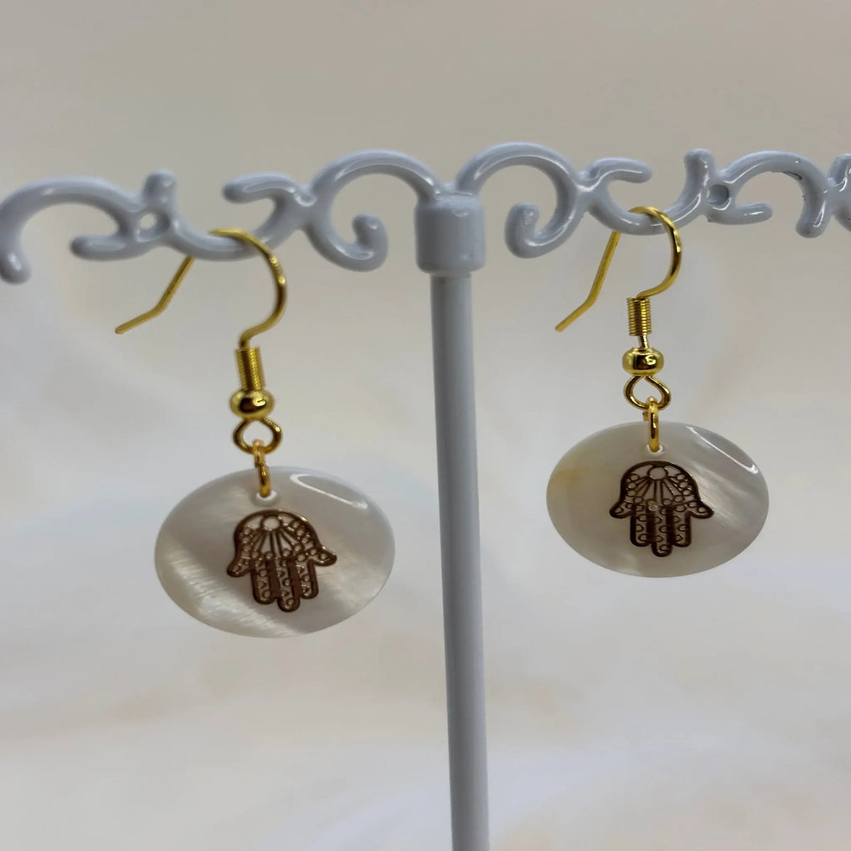 Une paire de boucles d'oreilles avec une pastille nacrée et dessin d'une main de Fatma