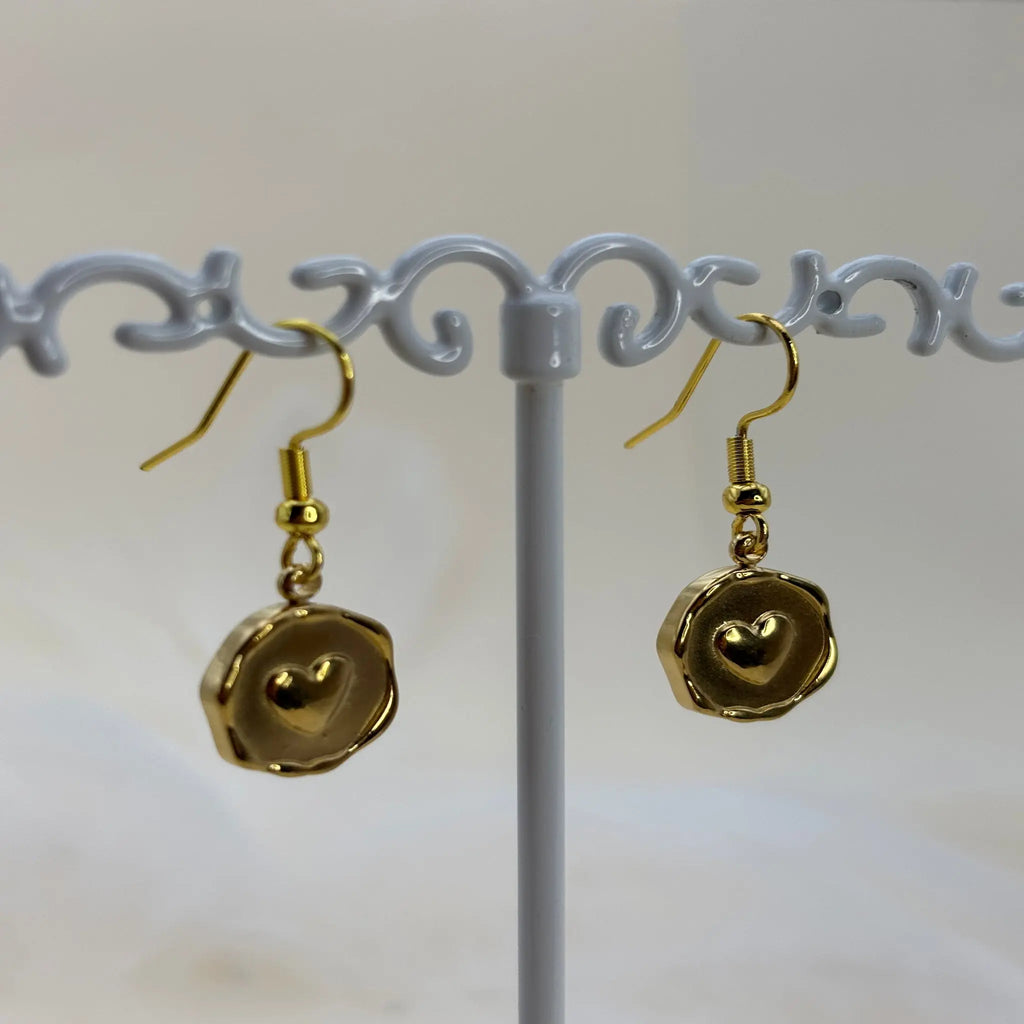 Une paire de boucles d'oreilles dorées avec un coeur dans un pendentif