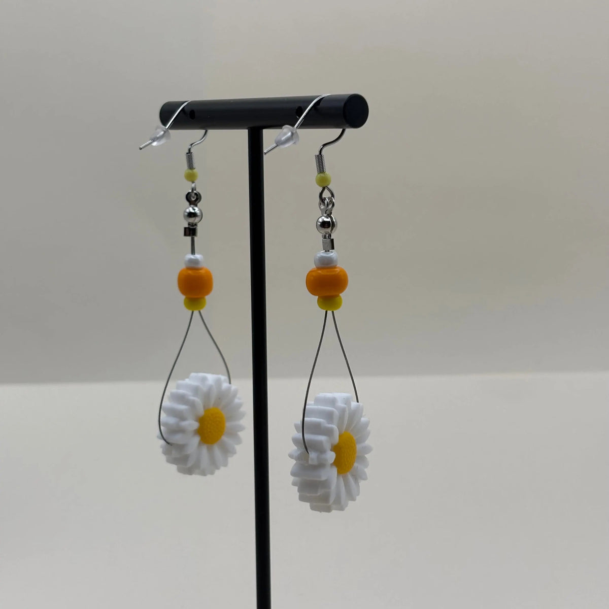 Une paire de boucles d'oreilles artisanales créoles avec perles oranges jaune et blanche et fleur de marguerite 