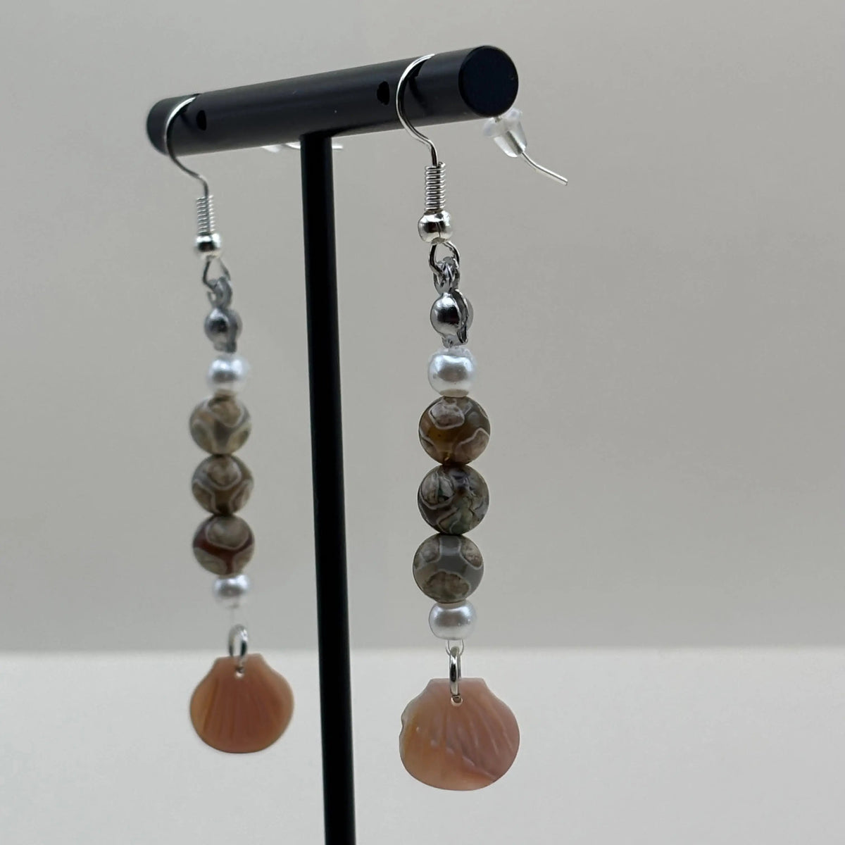 Une paire de boucles d’oreilles pendantes avec attache argentée et breloque en forme de coquillage nacré et perles colorées marbrées