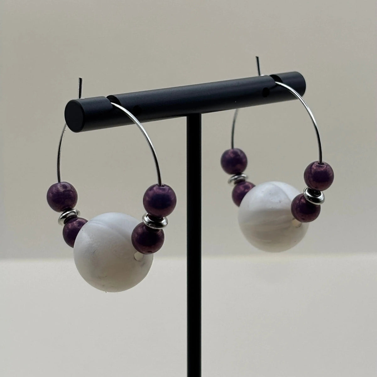 Des boucles d’oreilles créoles argentées avec grosse perles blanche et quatre perles violettes
