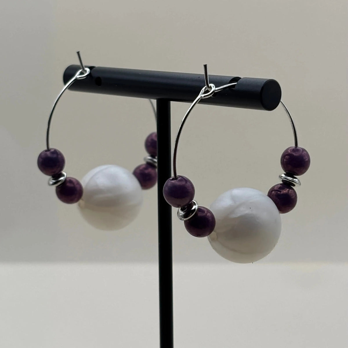 Une paire de boucles d’oreilles créoles argentées avec grosse perles blanche et quatre perles violettes