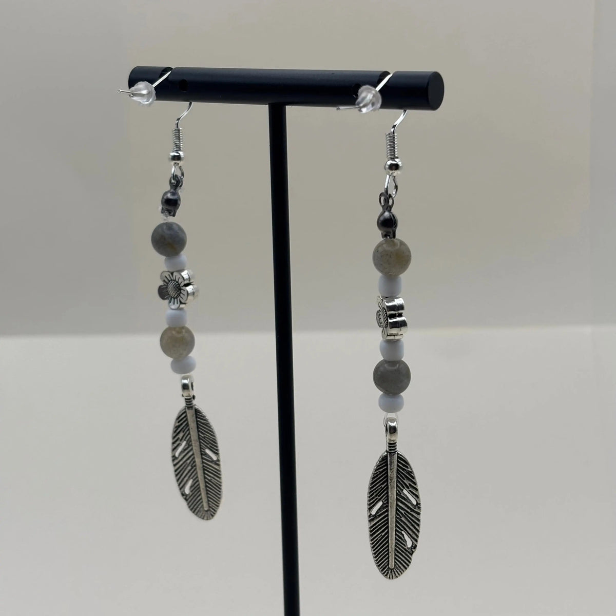 Des boucles d’oreilles pendantes avec attache argentée breloque argentée en forme de plume et fleur et perles pastels 