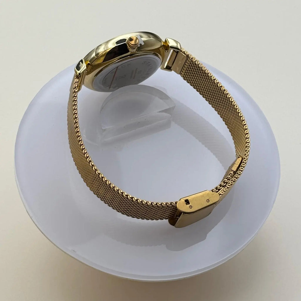 Vue de coté d'une montre pour femme bracelet doré cadran blanc irisé orné de strass sur le pourtour