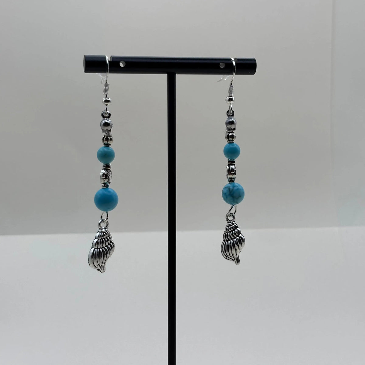 Boucles d’oreilles pendantes avec attache argentée et une breloque en forme de coquillage et des perles bleues