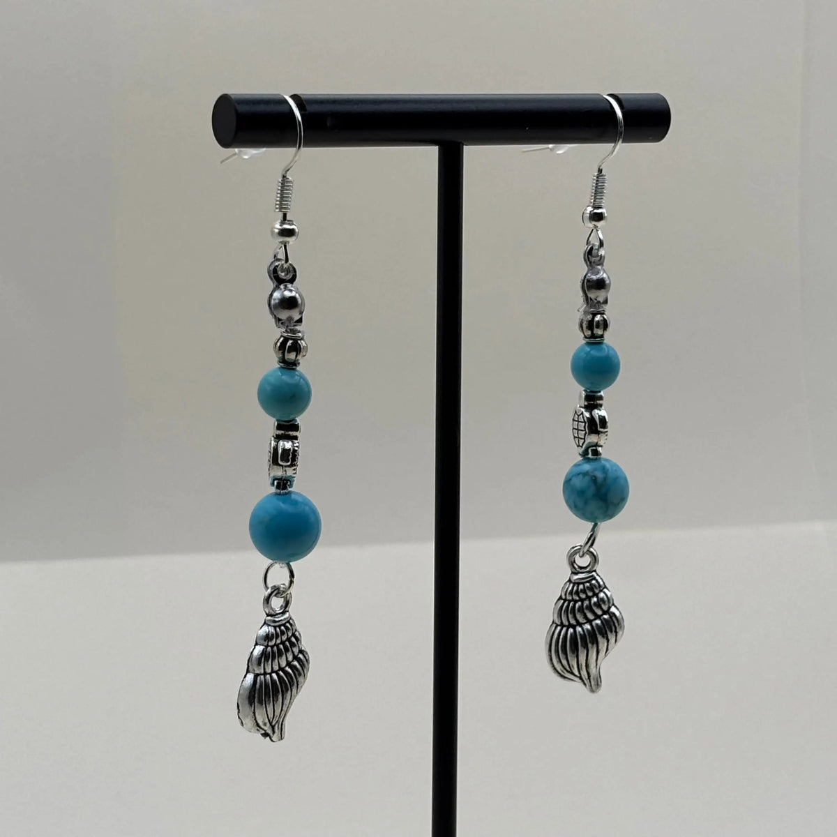 Des boucles d’oreilles pendantes avec attache argentée et une breloque en forme de coquillage et des perles bleues