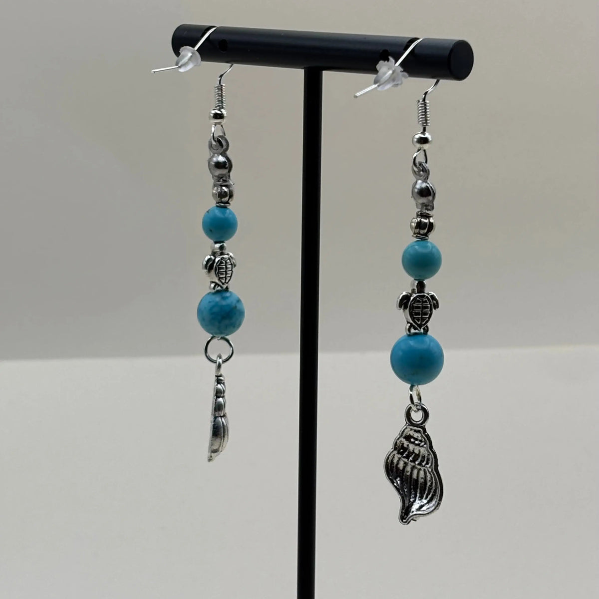 Une paire de boucles d’oreilles pendantes avec attache argentée et une breloque en forme de coquillage et des perles bleues