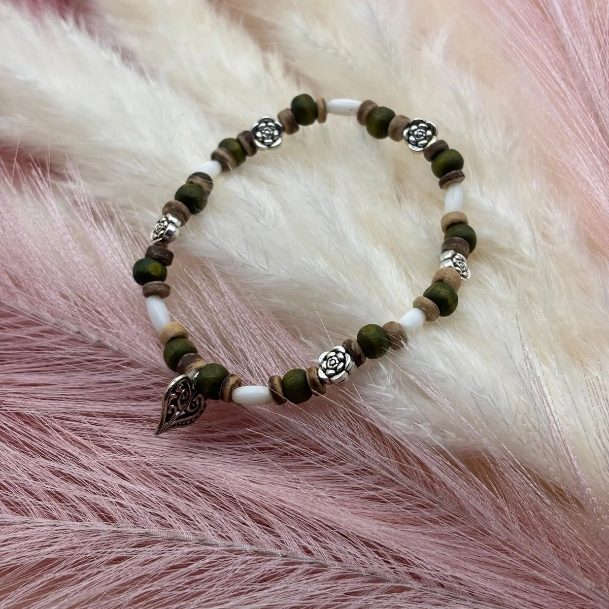 Vue de près d'un bracelet en perles artisanal avec breloque cœur et fleurs et des perles en bois sur élastique