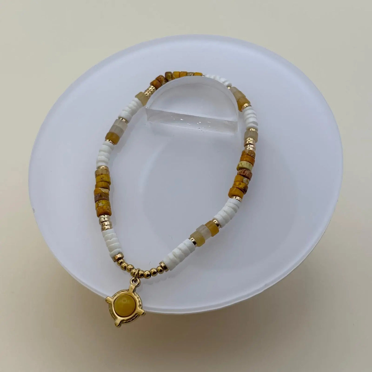 Bracelet doré avec des perles plates blanches et ambré et une breloque avec une pierre ronde marron clair dans un motif géométrique