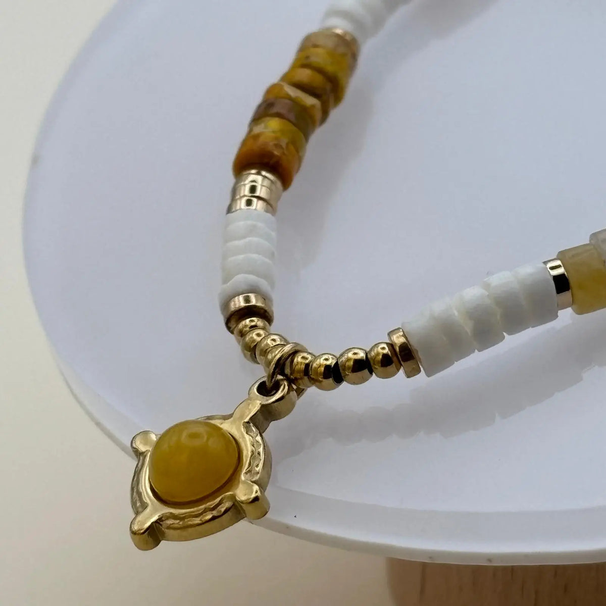 Bracelet doré avec des perles plates blanches et ambré et une breloque avec une pierre ronde marron clair