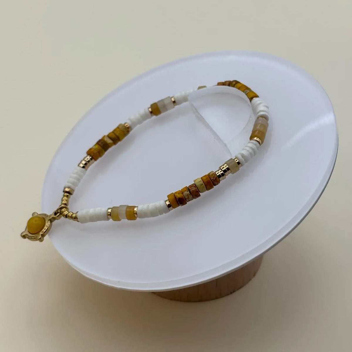 Bracelet doré avec perles plates blanches et ambré et une breloque avec une pierre ronde marron clair dans un motif géométrique