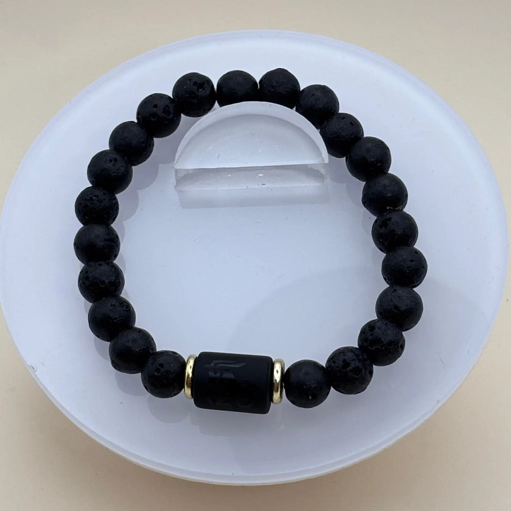 Bracelet en perles noires mates et lisses agrémenté d’un cylindre noir gravé encadré par deux anneaux dorés