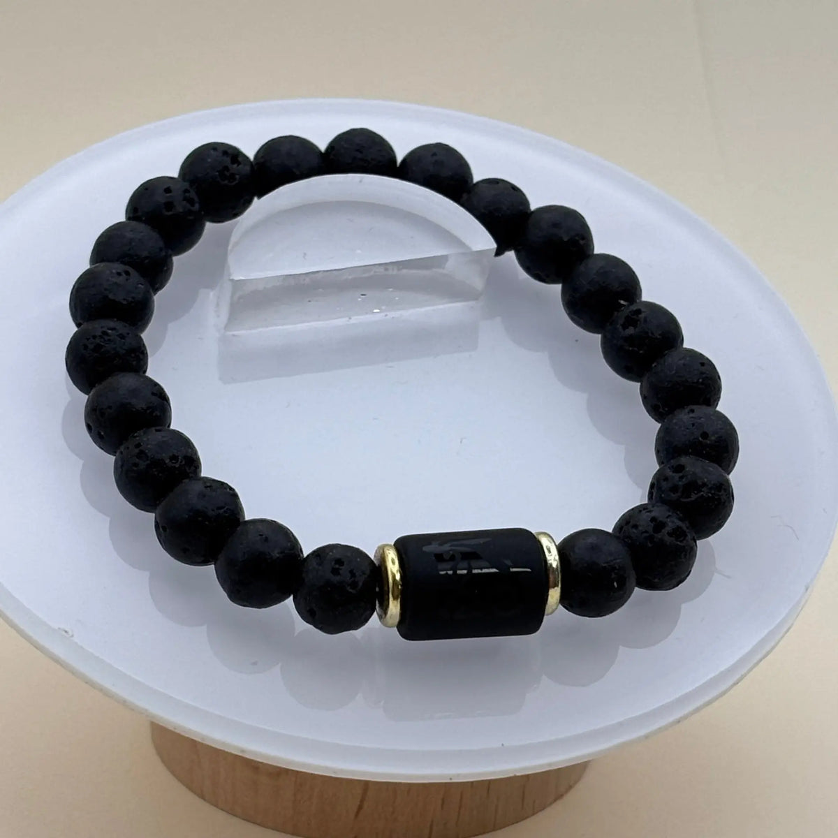 Bracelet composé de perles noires mates accompagné d’un cylindre noir gravé entouré de deux anneaux dorés