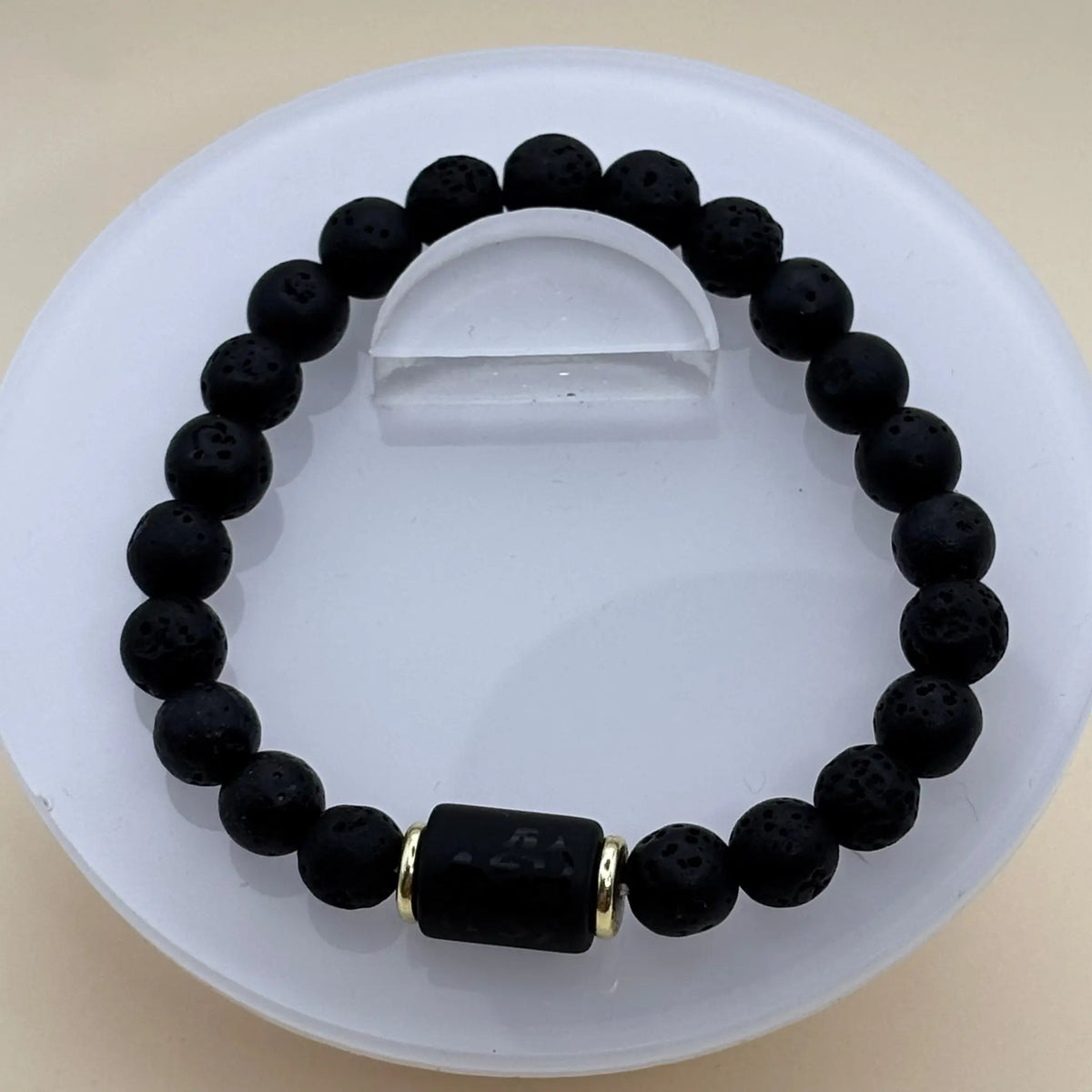 Bracelet en perles noires mates et lisses comportant un cylindre noir gravé entouré d’anneaux dorés