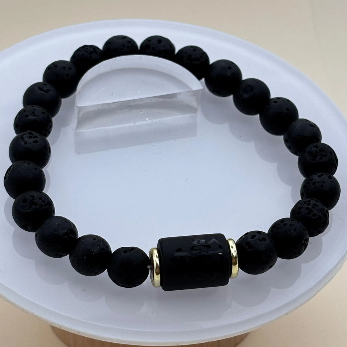 Bracelet en perles noires mates décoré d’un cylindre noir gravé encadré d’anneaux dorés