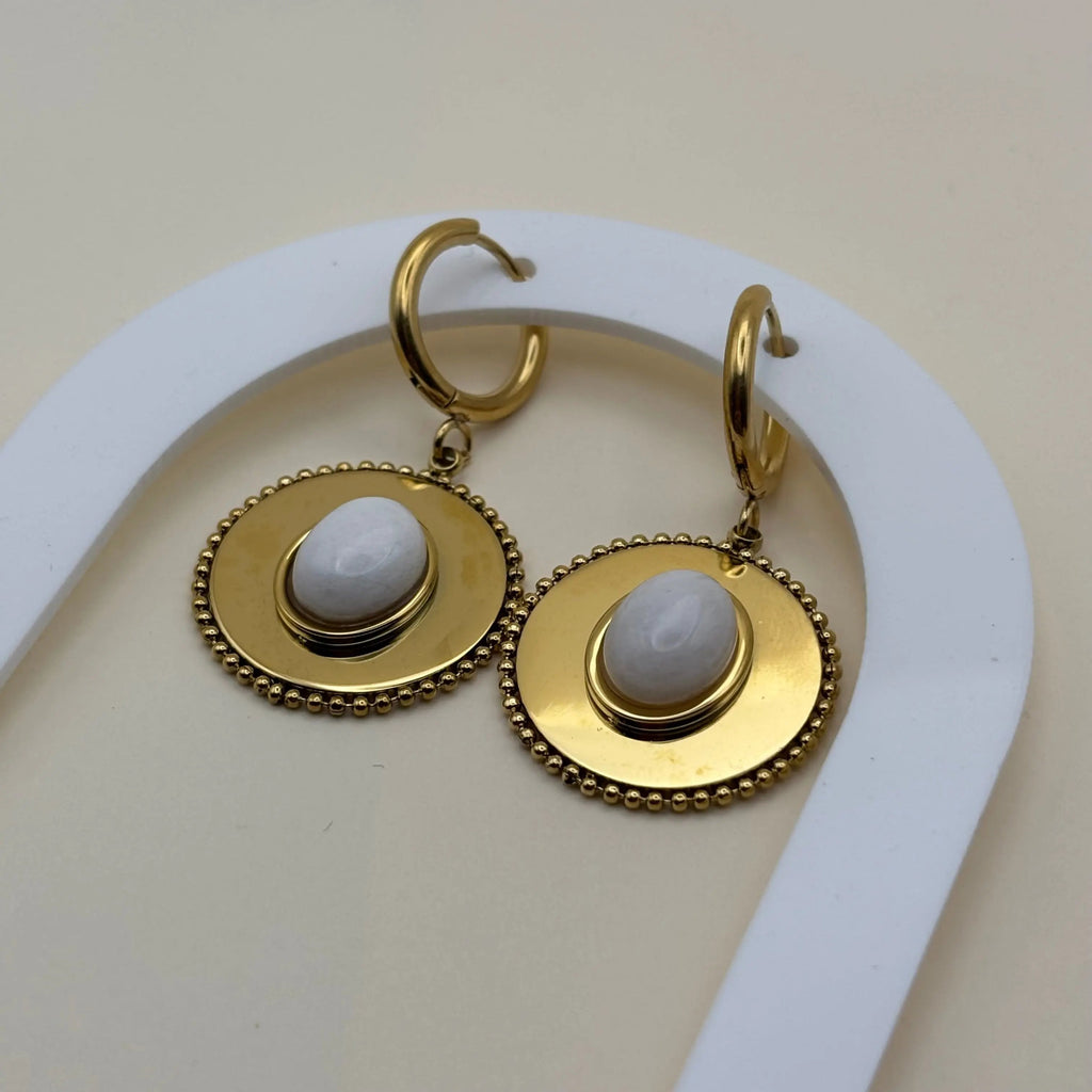 Une paire de boucles d'oreilles dorée pendantes avec cercle dorée et pierre façon camé blanc