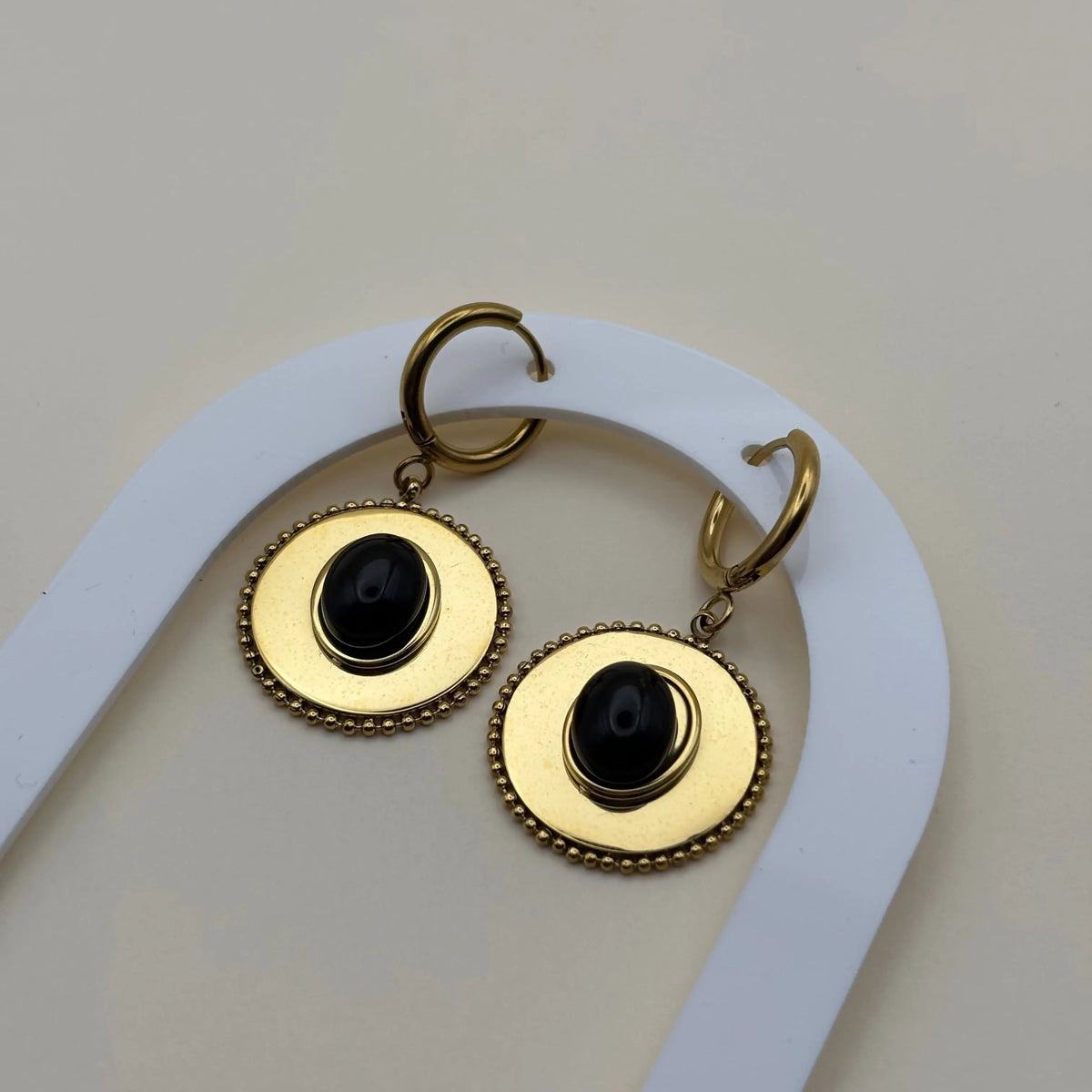 Une paire de boucles d'oreilles dorée pendantes avec cercle dorée et pierre façon camé noir