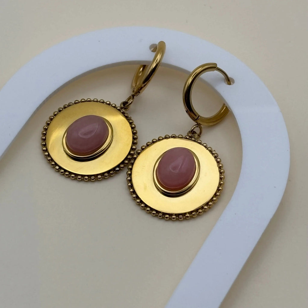 Une paire de boucles d'oreilles dorée pendantes avec cercle dorée et pierre façon camé rose