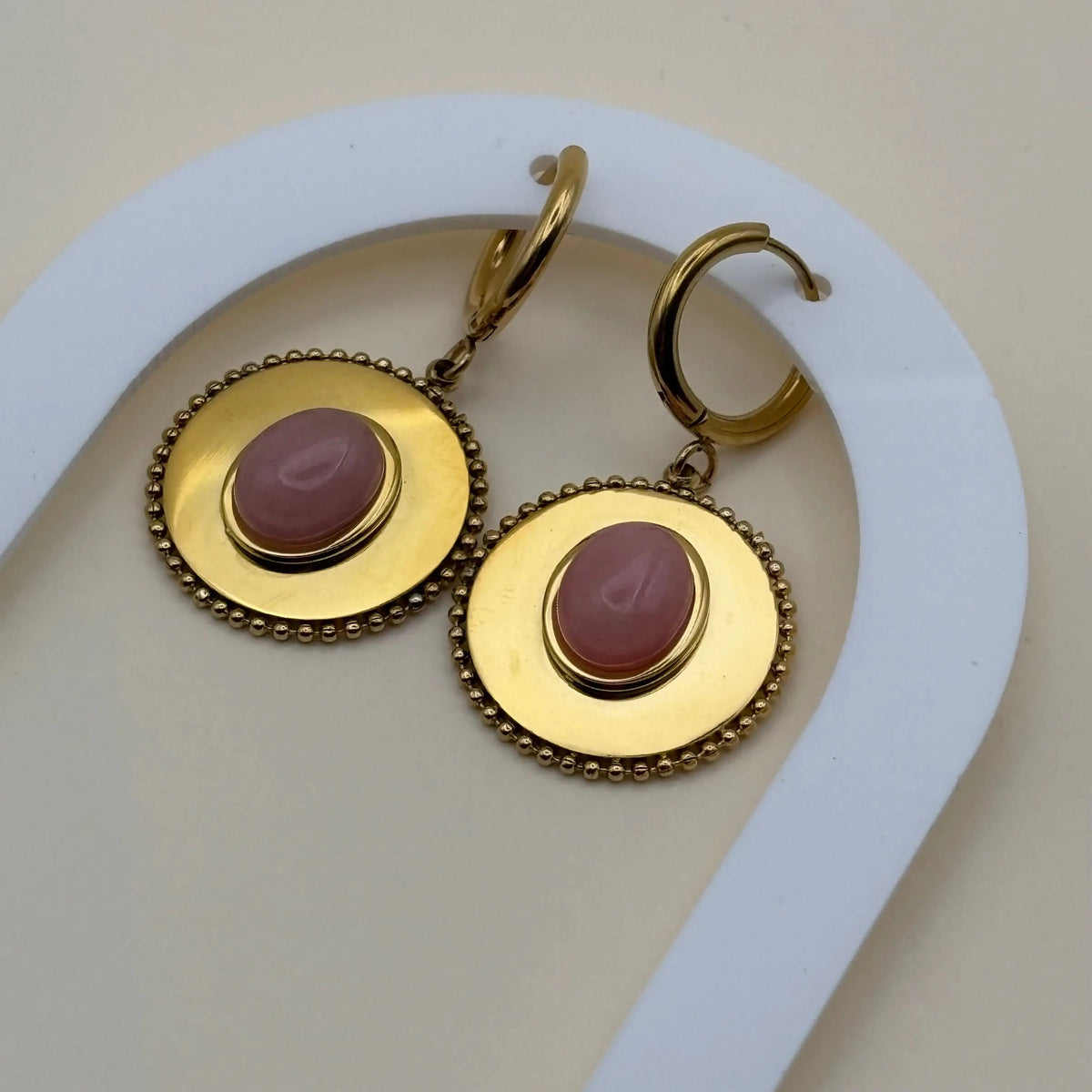 Une paire de boucles d'oreilles dorée pendantes avec cercle dorée et pierre façon camé rose